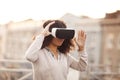 Young modern mixed-race woman in VR goggles headset exploring virtual reality outdoors