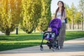 Young modern mom with baby son in stroller walking in Sunny Park. Concept of the joy of motherhood and autumn mood Royalty Free Stock Photo