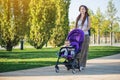 Young modern mom with baby son in stroller walking in Sunny Park. Concept of the joy of motherhood and autumn mood Royalty Free Stock Photo