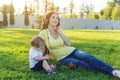 Young modern mom playing in a green meadow with her cute baby son in a Sunny Park. Concept of the joy of motherhood Royalty Free Stock Photo