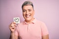 Young modern romantic man holding heart shape drawing over isolated pink background with a happy face standing and smiling with a