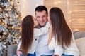 Young mom, father, and their little daughter lovely sitting near Christmas tree on sofa. Royalty Free Stock Photo