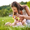 Young mom and her baby daughter playing together with a rattle in the grass outddors - Carefree childhood and family concept Royalty Free Stock Photo