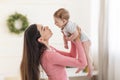 Young mom lifting her adorable newborn baby in air while standing in bedroom at home, holding him in hands, free space Royalty Free Stock Photo