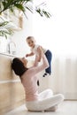 Young mom lifting her baby son up in air, sitting on kitchen floor Royalty Free Stock Photo