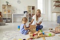 Young mom playing with cute little son and teaching him to build toy house in cozy modern apartment