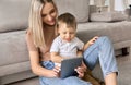 Young mom sitting on floor at home with kid watching movies on tablet. Royalty Free Stock Photo