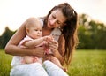 Young mom sitting in a park in the grass with his little baby daughter on her lap - 20s wife plays with his child while the baby Royalty Free Stock Photo