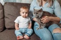 Young mommy, daughter and cat sits on the couch in the home interior