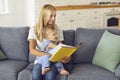 Young mommy reading book of fairy tales to her little child sitting on couch at home Royalty Free Stock Photo
