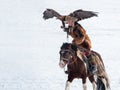 Young Mongolian eagle on the horse huntress setting free her eagle as it takes flight to go hunting against a white sunny snow