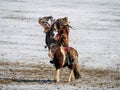 Young Mongolian eagle huntress riding a horse unleashing her eagle as it takes off to go hunting against a background of white