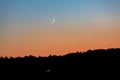 A young moon on an orange-blue sunset sky over a dark forest. Horizontal orientation. High quality photo Royalty Free Stock Photo