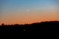 A young moon on an orange-blue sunset sky over a dark forest. Horizontal orientation. High quality photo Royalty Free Stock Photo
