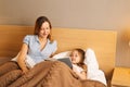 Young mother and adorable daughter reading children book together lying in bed before going to sleep Royalty Free Stock Photo