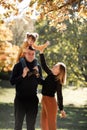 Young mother and adorable little daughter sitting on fathers shoulders are walking outdoors at autumn park. Dad, mom and Royalty Free Stock Photo