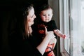 Young mother and baby girl at home looking by the window. Baby girl wearing Halloween clothes. Family lifestyle indoors Royalty Free Stock Photo