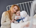 Young mother and baby lying on the bed playing with a bear toy Royalty Free Stock Photo