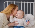 Young mother and baby lying on the bed playing with a bear toy Royalty Free Stock Photo