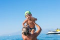 Young mother in black sunglasses and smiling baby boy son in the green baseball cap playing in the sea in the day time. Positive h Royalty Free Stock Photo