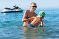 Young mother in black sunglasses and smiling baby boy son in green baseball cap playing in the sea in the day time. Positive human Royalty Free Stock Photo