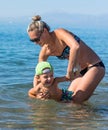 Young mother in black sunglasses and smiling baby boy son in green baseball cap playing in the sea in the day time. Positive human Royalty Free Stock Photo