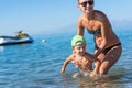Young mother in black sunglasses and smiling baby boy son in green baseball cap playing in the sea in the day time. Positive human Royalty Free Stock Photo