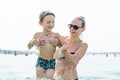 Young mother in black sunglasses and smiling baby boy son in green baseball cap playing in the sea in the day time. Positive human Royalty Free Stock Photo