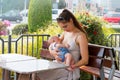 Young mother is breastfeeding cute little baby outside at public place, nursing in restaurant, busy street with cars behind them Royalty Free Stock Photo