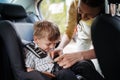 Young mother buckling toddler into child safety car seat.