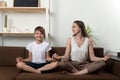 Young mother and child boy doing yoga, meditate in lotus position on couch