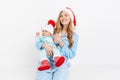 A young mother, on Christmas day gives a gift to a newborn child, a girl holds a baby in her arms in a Christmas hat Royalty Free Stock Photo