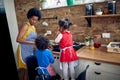 Young mother cooking dinner with her two young children in a domestic kitchen standing by the stove, frying veggies in a pan Royalty Free Stock Photo