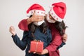 Young mother covering eyes to her daughter giving a red present for christmas wearing face mask and santa hat Royalty Free Stock Photo