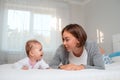 Young mother and cute baby lying on the bed on their stomachs, looking at each other happily. Concept of motherhood and child care Royalty Free Stock Photo