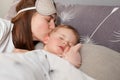 Young mother dark haired woman kissing sweet little baby, cute kid laying near mom and sleeping while parent kissing her, home Royalty Free Stock Photo