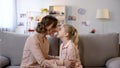 Young mother and daughter nuzzling sitting on sofa, close family relations, love