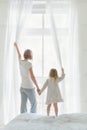 Young mother with daughter opening window curtains