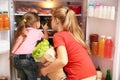 Young mother and daughter with paper bag full of food near refrigerator