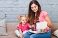 Young mother and daughter of two years old blonde use laptop computer laptop white with bright print sitting on couch indoors Royalty Free Stock Photo