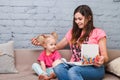 Young mother and daughter of two years old blonde use laptop computer laptop white with bright print sitting on couch indoors Royalty Free Stock Photo