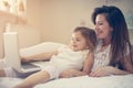 Young mother with daughter using laptop on bed at home. Royalty Free Stock Photo