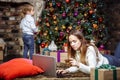 A young mother is doing online shopping with laptop and credit card while her daughter decorates the Christmas tree.