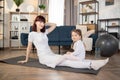 Young mother doing yoga exercise at home wearing white sportswear, with funny little daughter Royalty Free Stock Photo