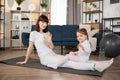 Young mother doing yoga exercise at home wearing white sportswear, with funny little daughter Royalty Free Stock Photo