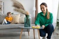 Young mother dusting off coffee table and tidying up at home while toddler son watching cartoon on cellphone Royalty Free Stock Photo