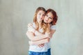 Young mother embracing her child. Woman and teenage girl relaxing in white bedroom near gray wall indoors. Happy family at home. Royalty Free Stock Photo