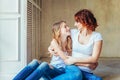 Young mother embracing her child. Woman and teenage girl relaxing in white bedroom near gray wall indoors. Happy family at home. Royalty Free Stock Photo