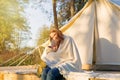 Young mother embracing her happy kid with a blanket while sitting near canvas bell tent in the forest Royalty Free Stock Photo