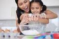 Young mother enjoying baking, bonding with her little daughter in the kitchen at home. Little latino girl smiling while